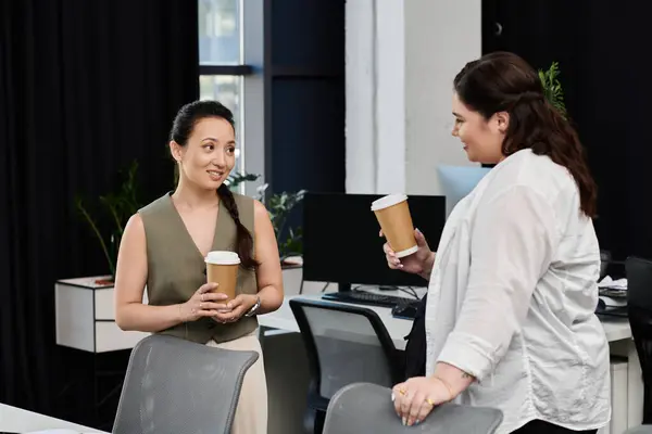 Two women engage in a lively conversation while enjoying coffee in a stylish workspace. — Stock Photo