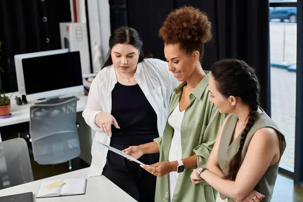 Three professional women discuss a project together, focused and engaged in their work. — Stock Photo