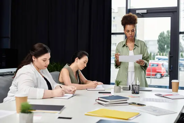 Three professional women engage in a focused discussion surrounded by office materials. — Stock Photo