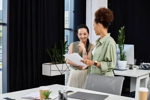 Two professional women discuss ideas while standing in a stylish office with greenery. — Stock Photo