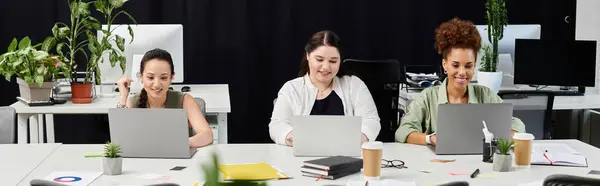 Three professional women work together intently on laptops in a stylish office setting. — Stock Photo