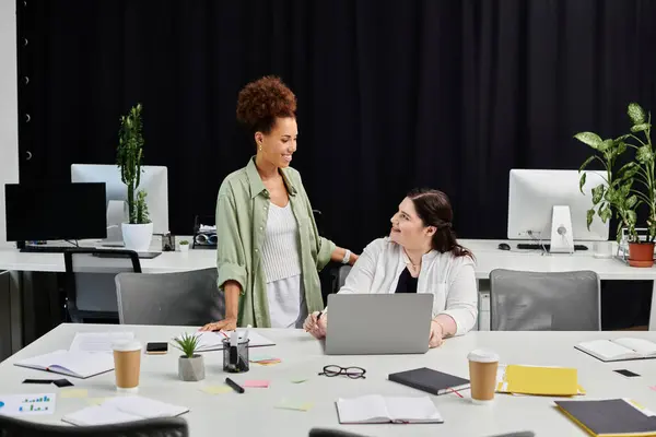Two professional women discuss ideas and strategies at a sleek office workspace filled with plants. — Stock Photo