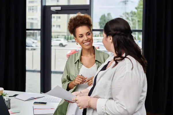 Deux femmes professionnelles discutent d'idées, mettant en valeur le travail d'équipe et la créativité dans un bureau élégant. — Photo de stock