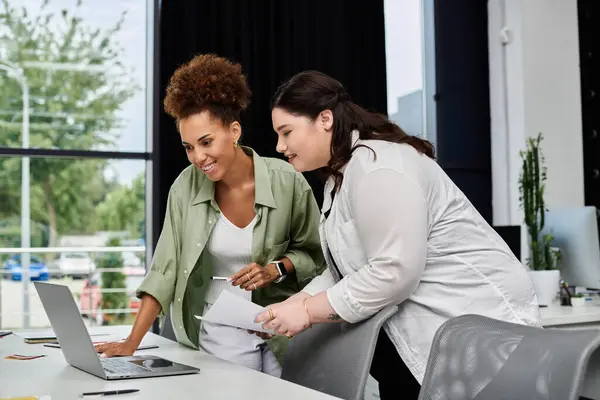 Two professional women discuss ideas together at a sleek office workspace by the window. — Stock Photo