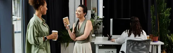 Two stylish businesswomen chat leisurely while holding coffee cups in a chic office space. — Stock Photo