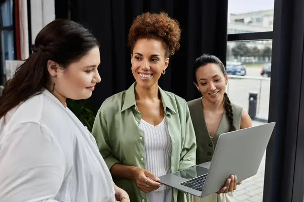 Three professional women share ideas while reviewing a laptop in an inviting office environment. — Stock Photo