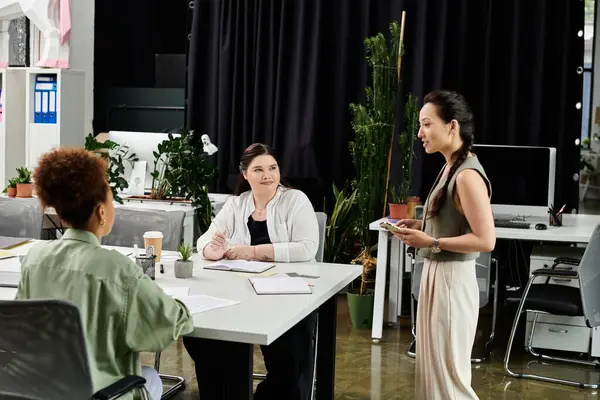 Three professional women engage in discussion around a table filled with documents and ideas. — Stock Photo