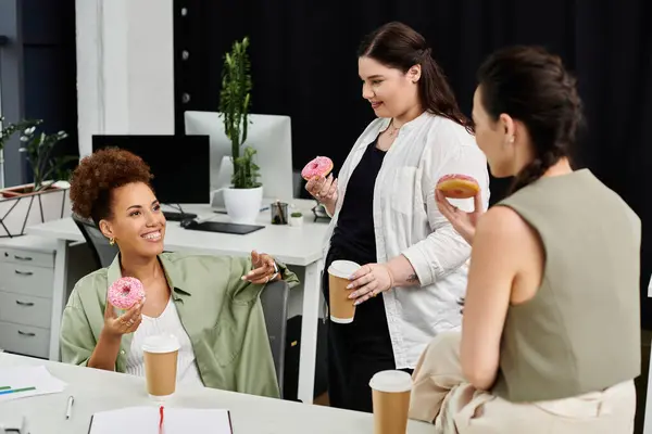 Tres mujeres con estilo participan en una animada discusión mientras disfruta del café y las rosquillas. - foto de stock