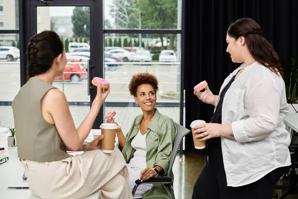 Three stylish professionals engage in a lively discussion while savoring treats and coffee. — Stock Photo