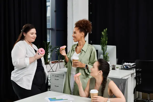 In an office, three stylish businesswomen share coffee and sweet treats while discussing ideas. — Stock Photo