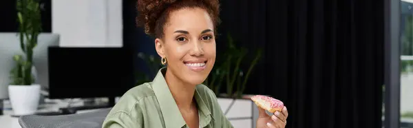 A confident businesswoman takes a moment to savor her snack in a contemporary office space. — Stock Photo