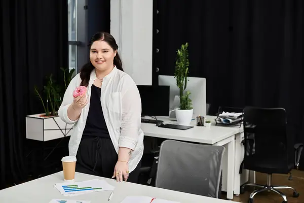 A businesswoman in a stylish outfit takes a break while holding a donut and coffee at her desk. — Stock Photo