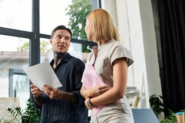 Two young professionals engage in a conversation while reviewing documents in the office. — Stock Photo