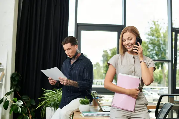 A cheerful coworker on the phone chats while a colleague reviews documents in their workspace. — Stock Photo