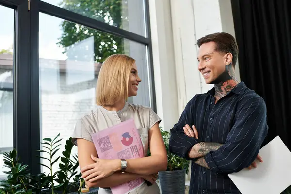Two young colleagues engage in a lively conversation while standing near large windows. — Stock Photo