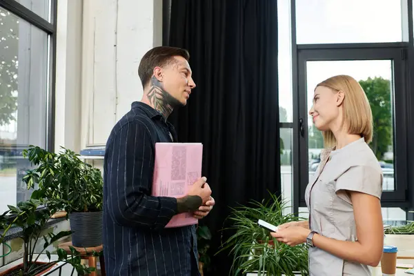 Two young professionals converse animatedly in a bright, plant filled workspace. — Stock Photo