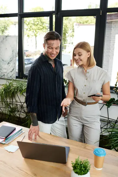 Two young professionals engage in a lively discussion beside a laptop in a modern office. — Stock Photo