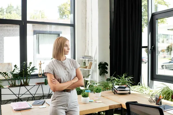 A young professional stands thoughtfully by the window, surrounded by plants and office supplies. — Stock Photo