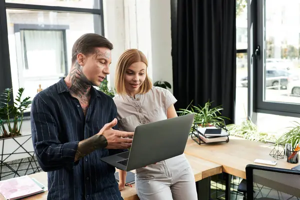 Two young coworkers engage in a discussion while working on a laptop in a modern office. — Stock Photo