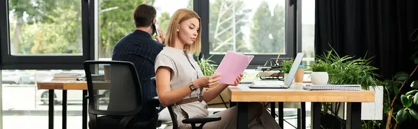 A young woman reviews documents while a colleague makes a call in a bright office space. — Stock Photo