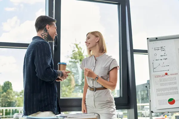 Two coworkers enjoy a lively discussion while standing in a modern office filled with natural light. — Stock Photo