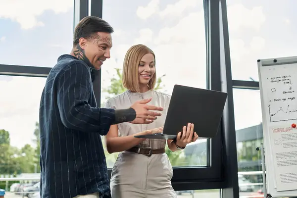 Two young colleagues share ideas while reviewing work on a laptop in a bright office environment. — Stock Photo