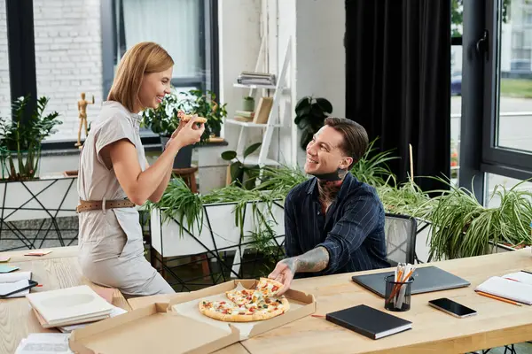 Two young colleagues enjoy lunch together, sharing pizza and smiles in a vibrant workspace. — Stock Photo