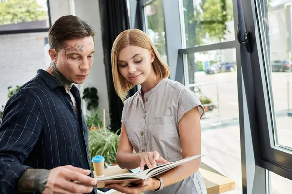 Two young colleagues discuss ideas and review documents while standing by large windows. — Stock Photo