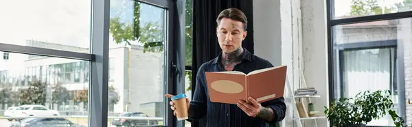 A young professional reviews notes while holding a coffee cup in a vibrant office environment. — Stock Photo