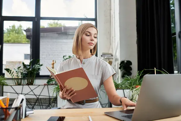 A focused team member reviews notes while engaging with a laptop in a vibrant office setting. — Stock Photo