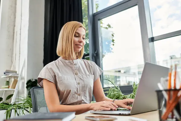 Un joven profesional se involucra con su computadora portátil, rodeada de un elegante entorno de oficina. - foto de stock