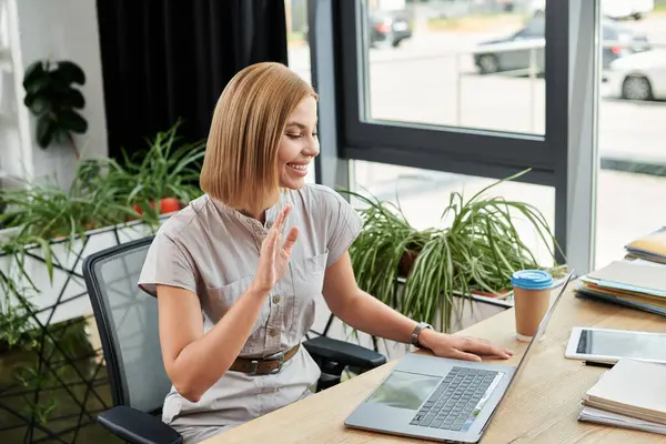 A cheerful young professional waves while participating in an online meeting at work. — Stock Photo