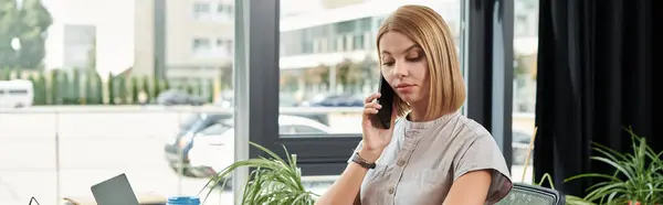 A young woman is focused on a phone conversation while working in a bright office. — Stock Photo