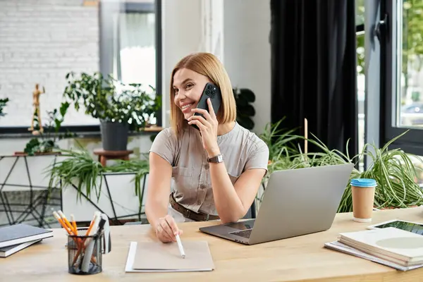 A cheerful coworker participates in a phone call, smiling and enjoying a vibrant office atmosphere. — Stock Photo