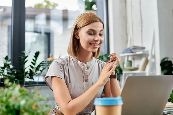 A cheerful woman engages with her laptop while surrounded by greenery and inspiring decor. — Stock Photo