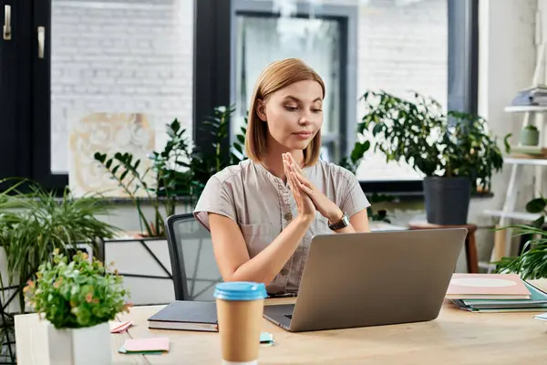A young professional focuses on her laptop while surrounded by greenery in a modern workspace. — Stock Photo