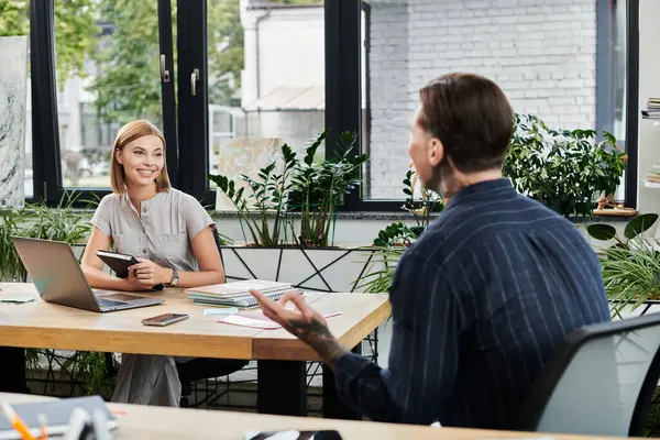 Two young professionals share ideas and collaborate in a bright, plant filled workspace. — Stock Photo