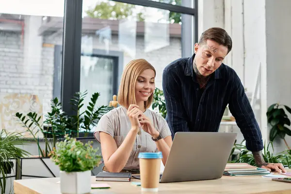 Two engaged coworkers discuss ideas and review work on their laptop in a lively office. — Stock Photo