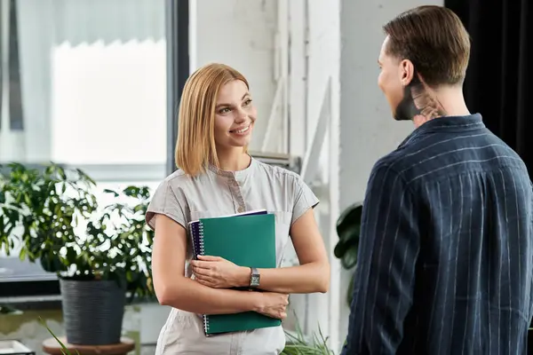 Two young professionals smile and share ideas, enhancing collaboration in a vibrant workplace. — Stock Photo