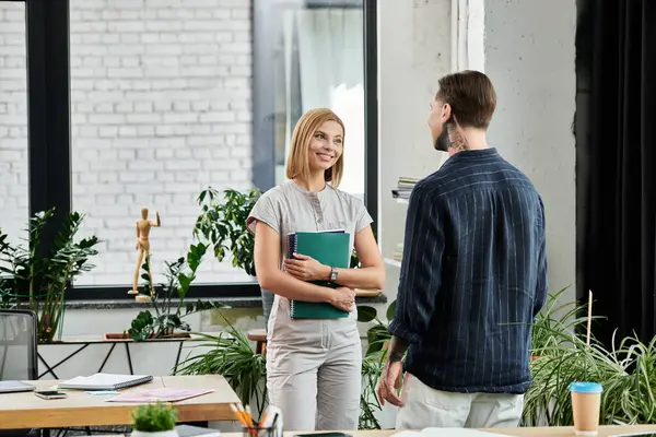 Two young colleagues converse warmly while standing amid greenery in their workspace. — Stock Photo