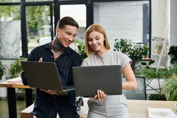 Two young coworkers share ideas while working on laptops in a bright, lively office space. — Stock Photo