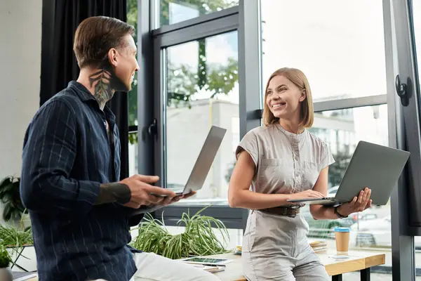 Two coworkers engage in a cheerful conversation while working on laptops in the office. — Stock Photo