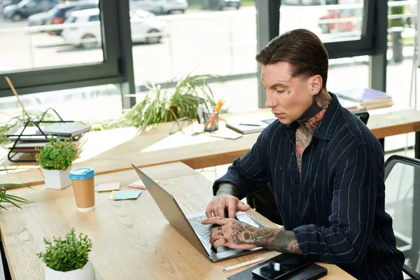 A focused coworker types on a laptop while surrounded by greenery and office supplies. — Stock Photo