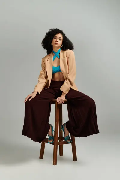 A fashionable woman showcases her bold style with a chic blazer and vibrant top while seated. — Stock Photo