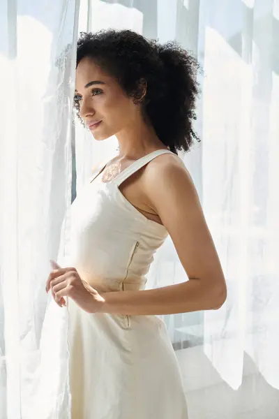 A fashionable woman stands gracefully in a beautiful outfit, lost in thought by the window. — Stock Photo