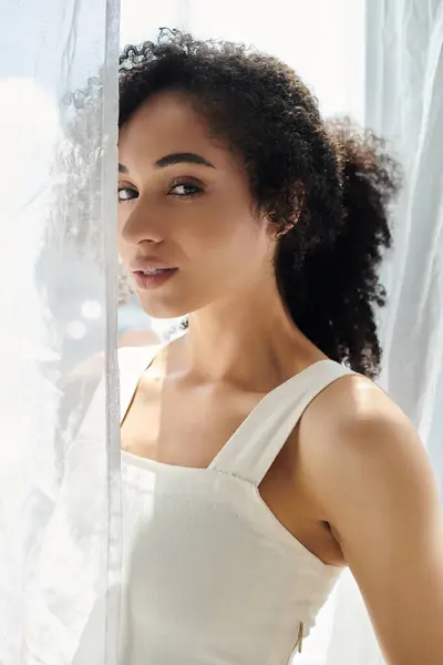 A woman with curly hair showcases her fashion sense while standing by a window. — Stock Photo