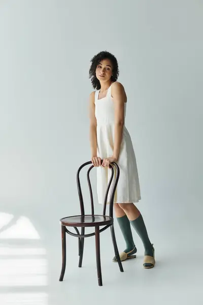 Eine atemberaubende Frau steht anmutig neben einem Stuhl und präsentiert trendige, moderne Kleidung. — Stockfoto