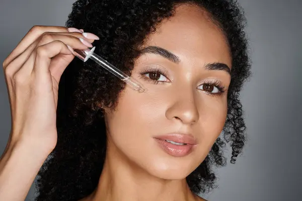 Una mujer con estilo aplica cuidadosamente un suero para el cuidado de la piel, destacando su radiante belleza y gracia. - foto de stock