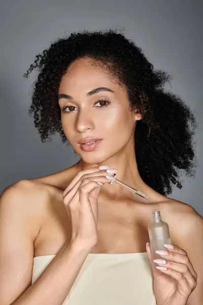 A stylish woman confidently showcases a beauty serum, gazing gracefully at the camera. — Stock Photo