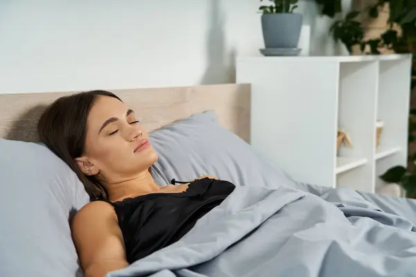 A young brunette woman with short stature rests comfortably in bed, surrounded by soft linens and home decor, savoring a serene moment. — Stock Photo